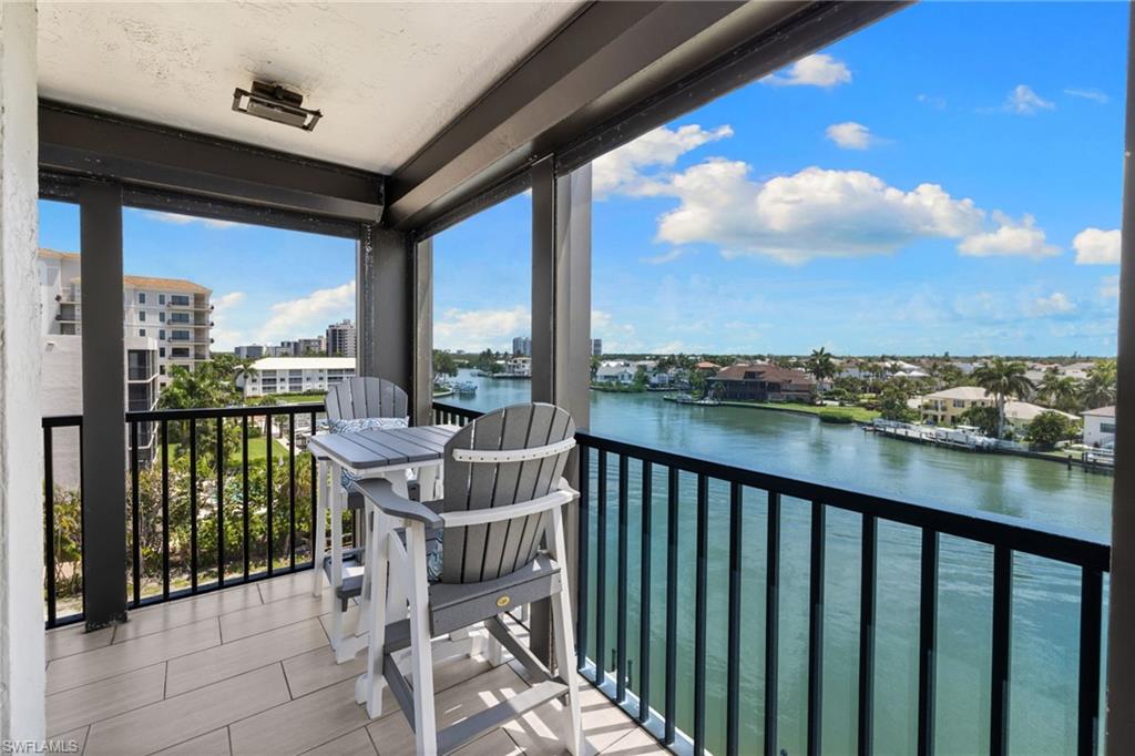 Balcony with tile flooring and black metal railings, overlooking a canal with residential properties