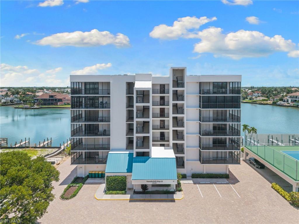 Modern multi-story building featuring expansive waterfront access, private balconies, and a paved parking area