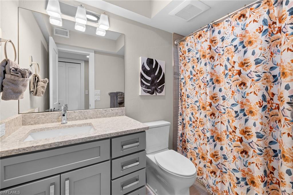Bathroom featuring a gray vanity with a stone-finish countertop, integrated sink, and contemporary hardware