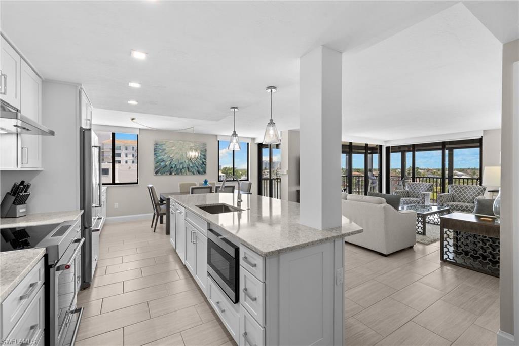 Open-concept kitchen featuring an island with an undermount sink, stainless steel appliances, light cabinetry, and light-toned tile flooring