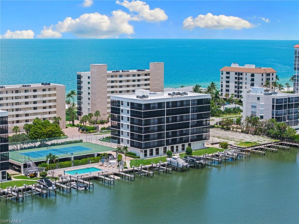 Waterfront complex featuring multiple residential buildings, a full-size tennis court, and an outdoor swimming pool