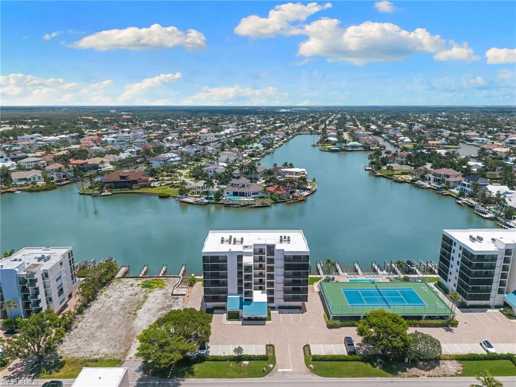 Waterfront multi-story building featuring multiple balconies, a ground-level tennis court, and an array of boat docks