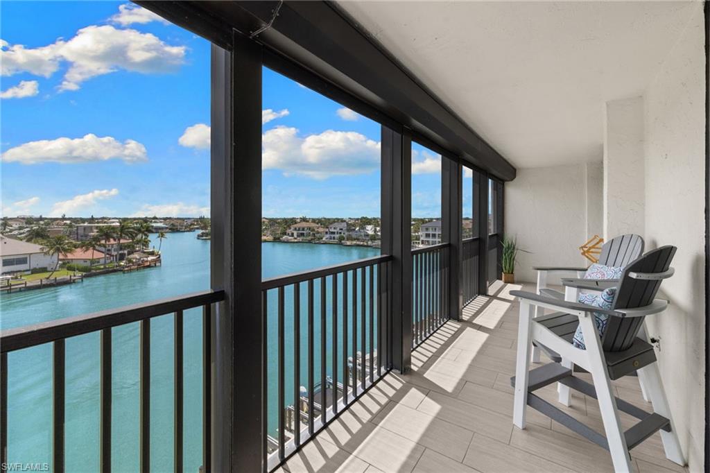 Spacious covered balcony featuring tile flooring and a black metal railing overlooking a wide canal with residential properties