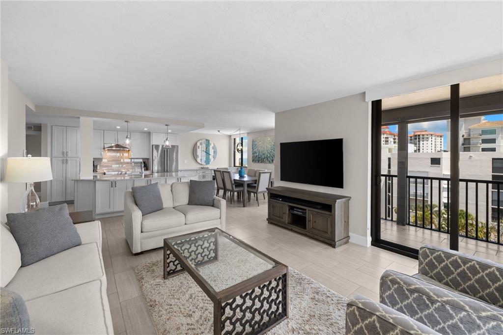 Open-concept living space featuring wood-finish flooring, a kitchen with light cabinetry and stainless steel appliances, a dining area, and a glass sliding door opening to a balcony with black railings