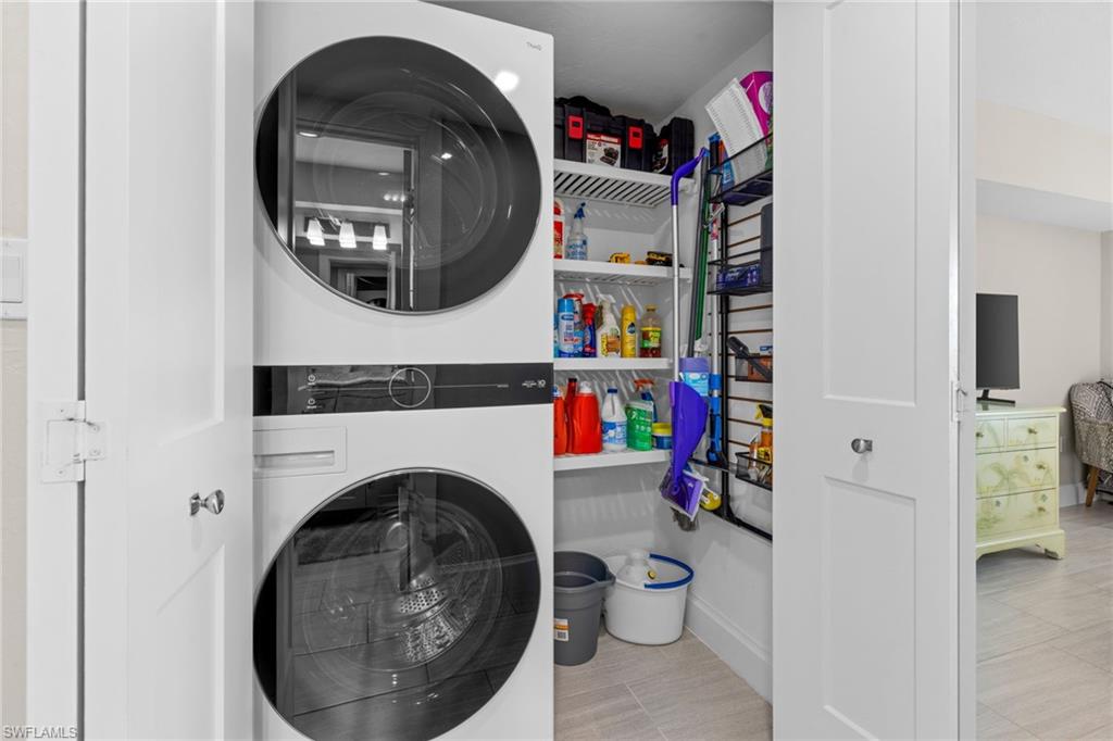 Utility closet featuring a stacked washer and dryer, white shelving, and tile flooring