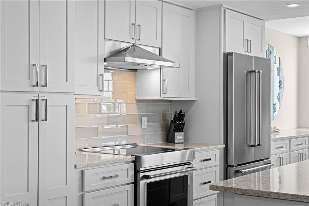 Modern kitchen featuring light gray shaker-style cabinetry, stainless steel appliances, a range hood, and a light-toned tile backsplash