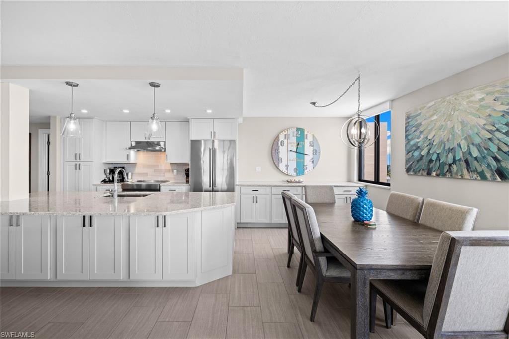 Open-concept kitchen and dining area featuring light wood-finish flooring, a kitchen island with stone countertops, white shaker cabinetry, stainless steel appliances, and a dining area with a modern chandelier
