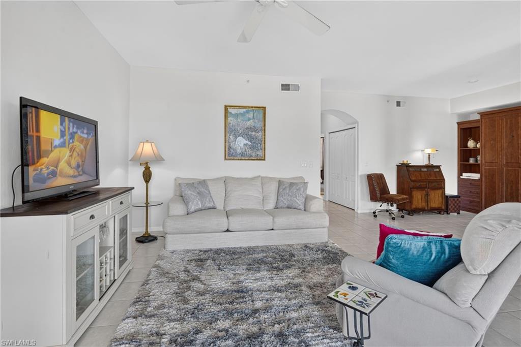Spacious living area featuring light-toned tile flooring, high ceilings, and a ceiling fan