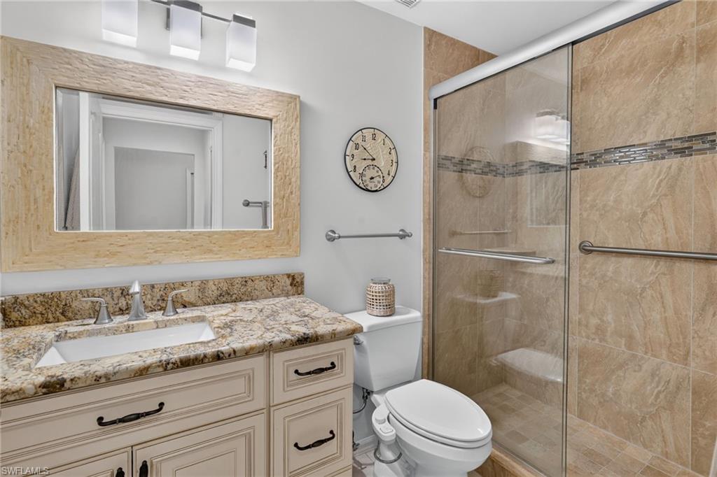 Bathroom featuring a glass-enclosed shower with tile surround and decorative mosaic band, a single vanity with stone countertop and integrated sink, a large framed mirror, and a modern light fixture