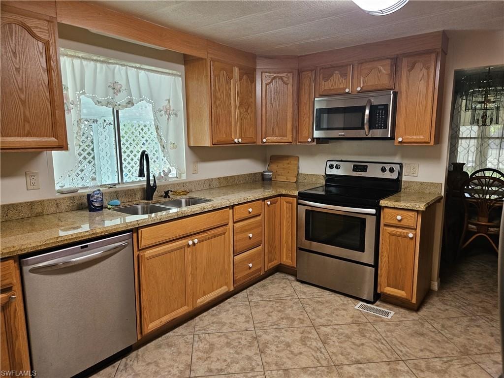 Kitchen with light tile patterned floors, stainless steel appliances, light stone countertops, and sink