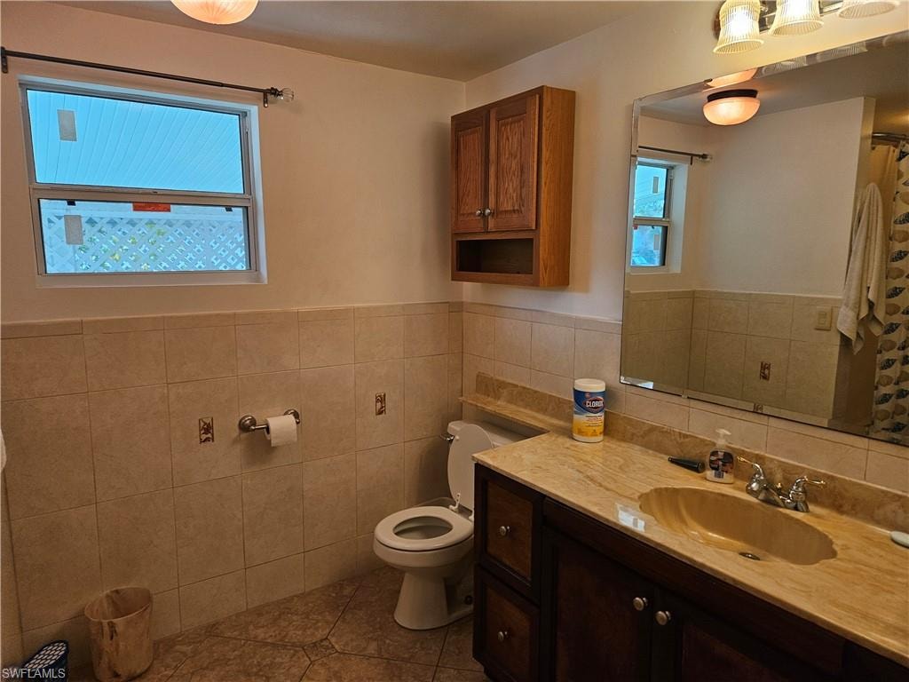 Bathroom with toilet, vanity, tile walls, and tile patterned flooring