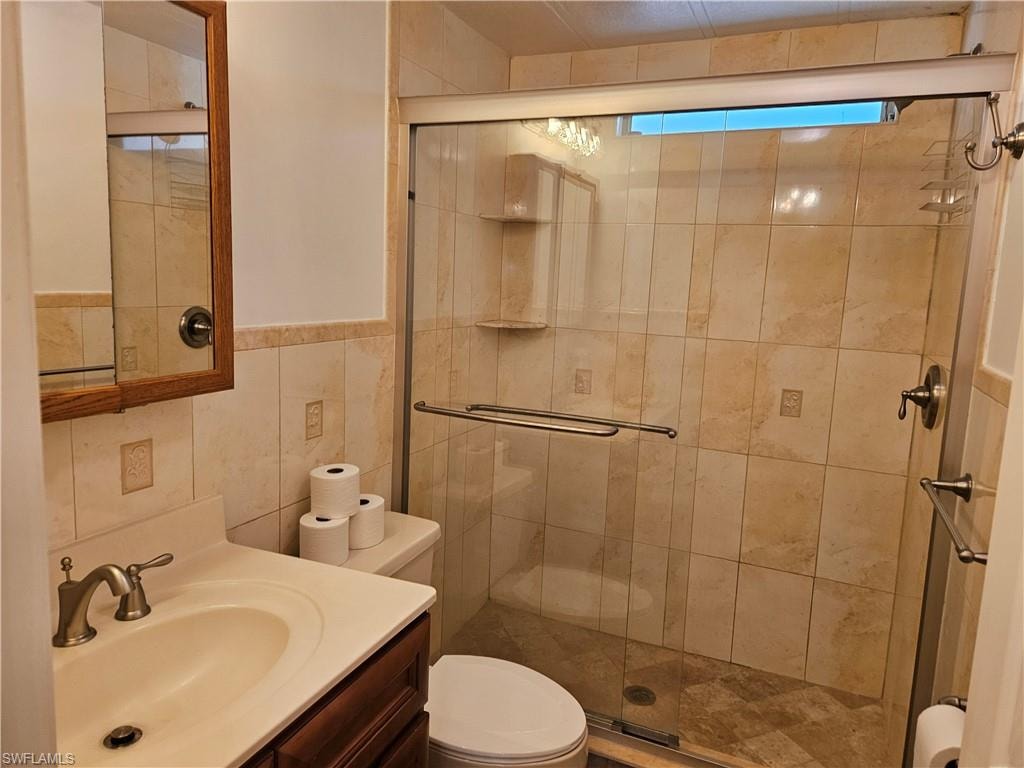 Bathroom with toilet, a shower with shower door, vanity, and tile walls