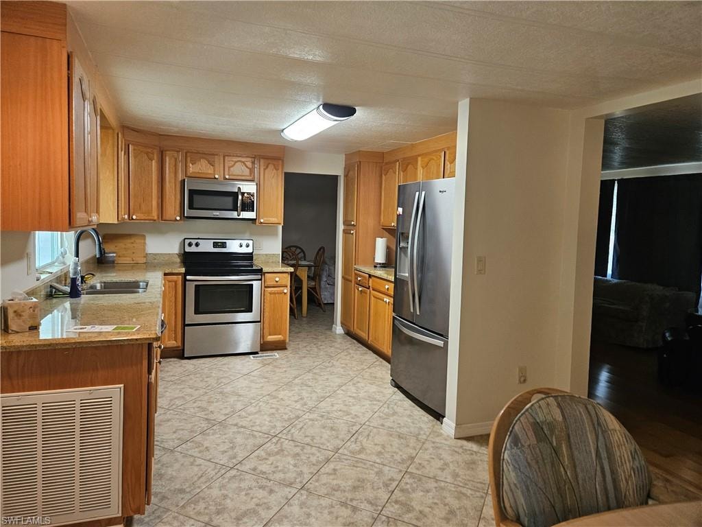 Kitchen with sink, appliances with stainless steel finishes, a textured ceiling, and light tile patterned flooring