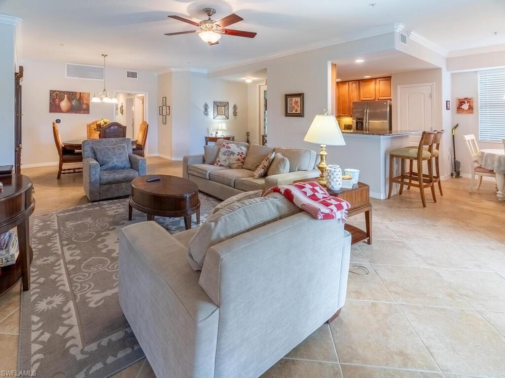 Living room featuring crown molding, light tile patterned floors, and ceiling fan with notable chandelier