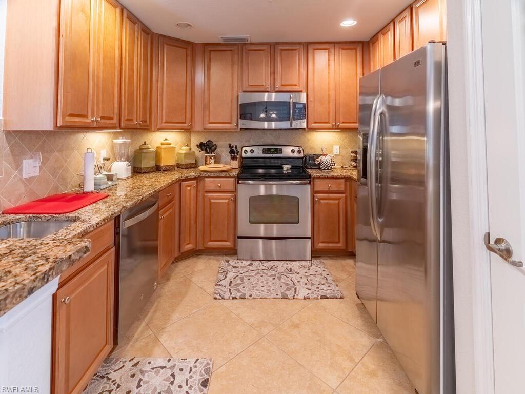 Kitchen featuring decorative backsplash, light stone countertops, stainless steel appliances, and light tile patterned floors