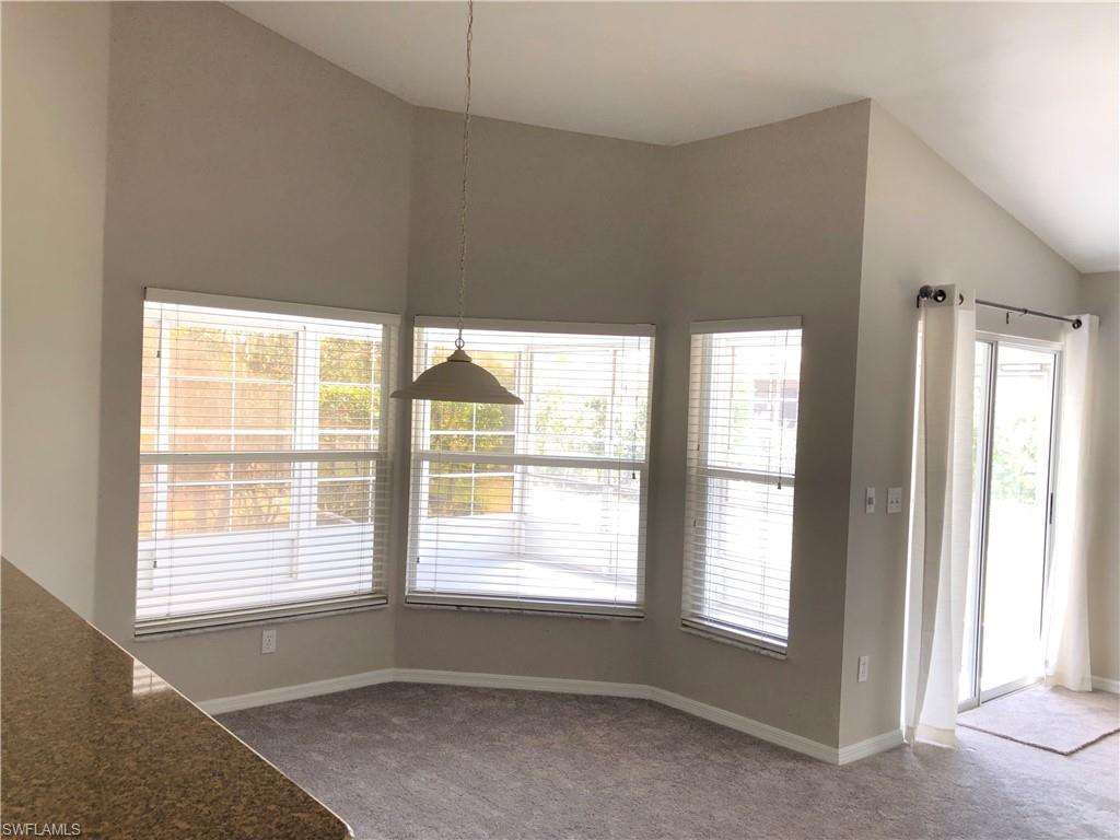 Carpeted dining nook with vaulted ceilings, a bay window with blinds, and a suspended light fixture