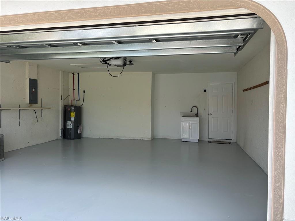 Spacious garage featuring a light gray finished floor, overhead door mechanism, utility sink with cabinet, and a water heater
