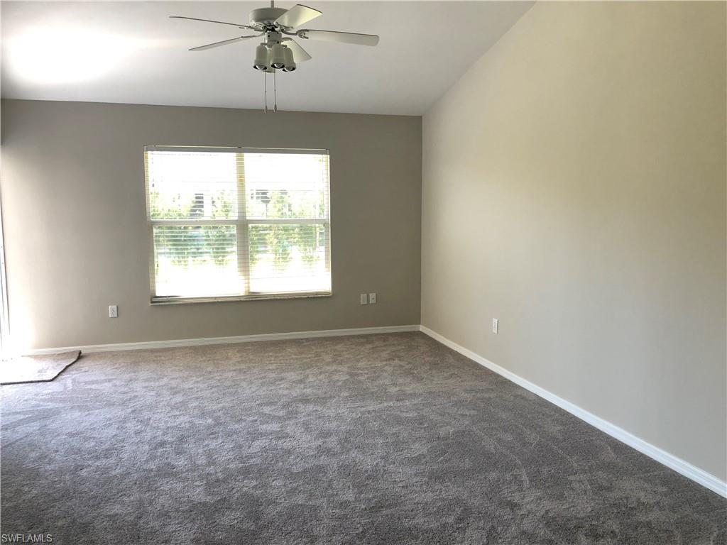 Spacious room featuring neutral-toned walls, gray carpet flooring, a large window with blinds, and a ceiling fan with integrated lighting
