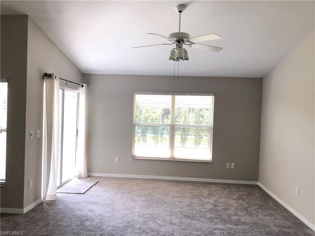 Vaulted ceilings enhance this carpeted room featuring a ceiling fan with light kit, a large window with blinds, and a sliding glass door