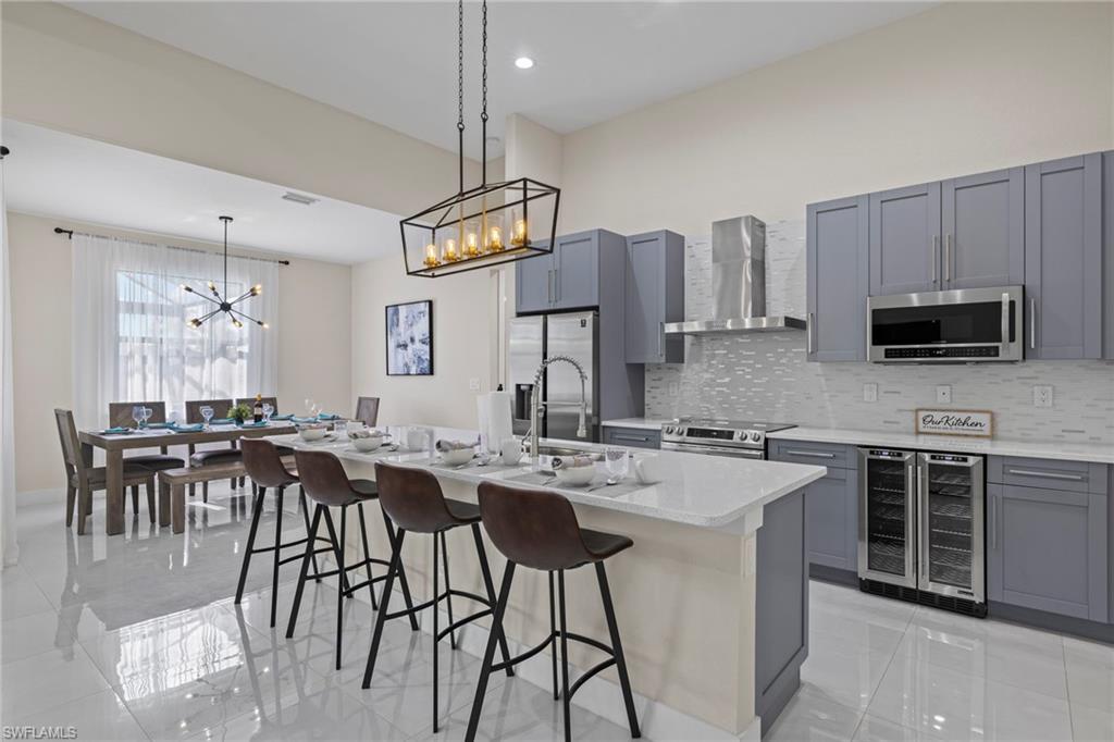 Kitchen with stainless steel appliances, wall chimney exhaust hood, wine cooler, an island with sink, and light tile patterned floors