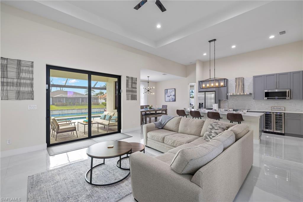 Tiled living room featuring sink, a high ceiling, ceiling fan with notable chandelier, a tray ceiling, and beverage cooler