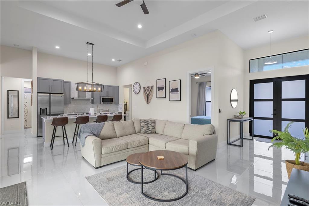 Tiled living room with ceiling fan with notable chandelier and a high ceiling