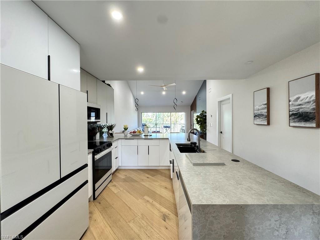 Kitchen featuring freestanding refrigerator, electric range oven, a sink, stainless steel microwave, and light wood-type flooring