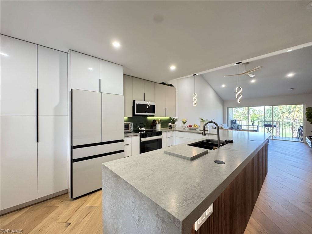 Kitchen with stainless steel microwave, black / electric stove, light wood-style floors, modern cabinets, and a sink