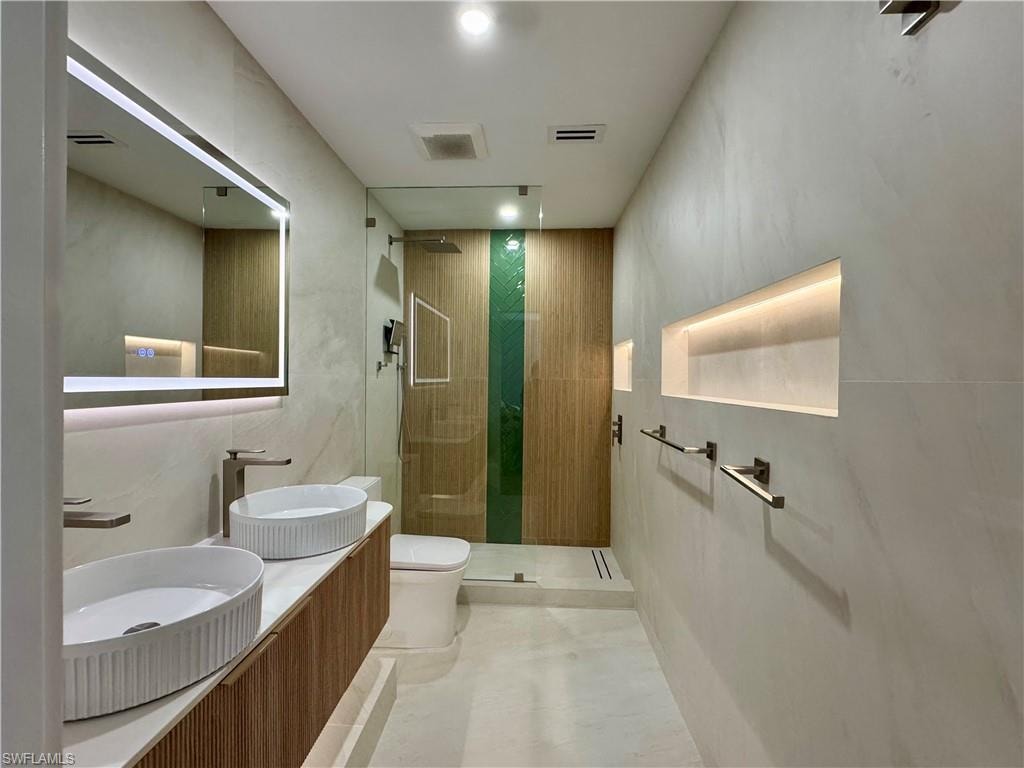 Bathroom featuring toilet, a stall shower, and double vanity
