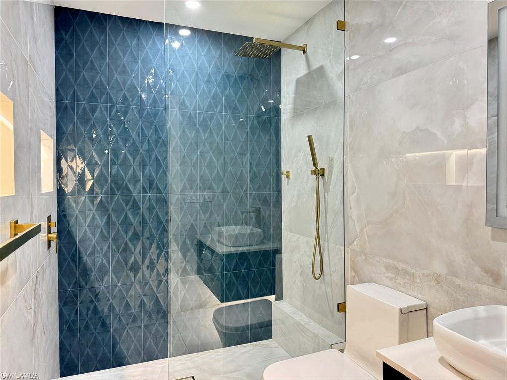 Bathroom with tile walls, vanity, toilet, a walk in shower, and recessed lighting