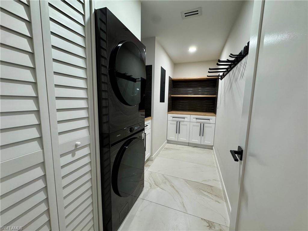 Washroom with stacked washer and clothes dryer, light marble finish floors, cabinet space, and baseboards