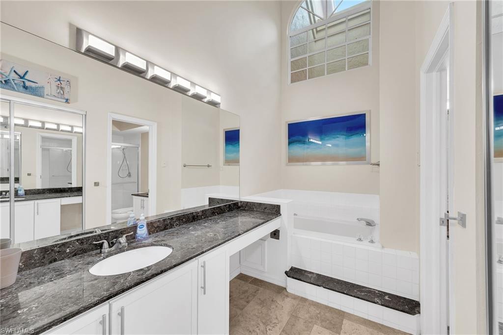 Spacious bathroom featuring an arched transom window, a deep soaking tub, and a dual vanity with a dark stone countertop