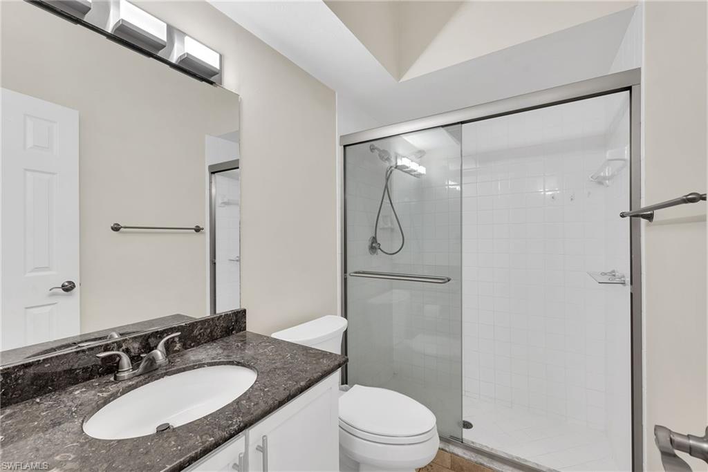 Bathroom featuring a vanity with a dark countertop and undermount sink, a large mirror, a chrome faucet, and a shower with sliding glass doors and white tiled walls