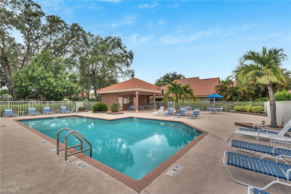 Resort-style pool area featuring a perimeter fence, a covered cabana, and mature landscaping