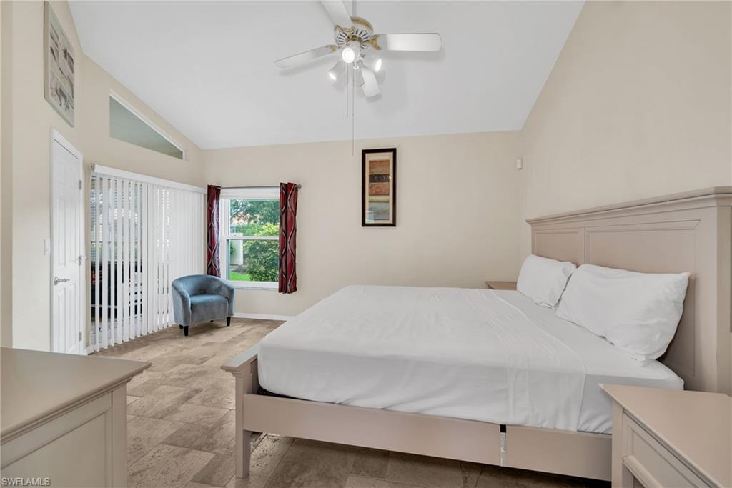 Vaulted ceiling bedroom with a ceiling fan, light-toned tile flooring, and a sliding glass door with vertical blinds
