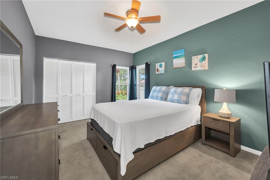 Carpeted room featuring a ceiling fan with integrated lighting, a louvered bi-fold closet, and dual windows with dark drapery