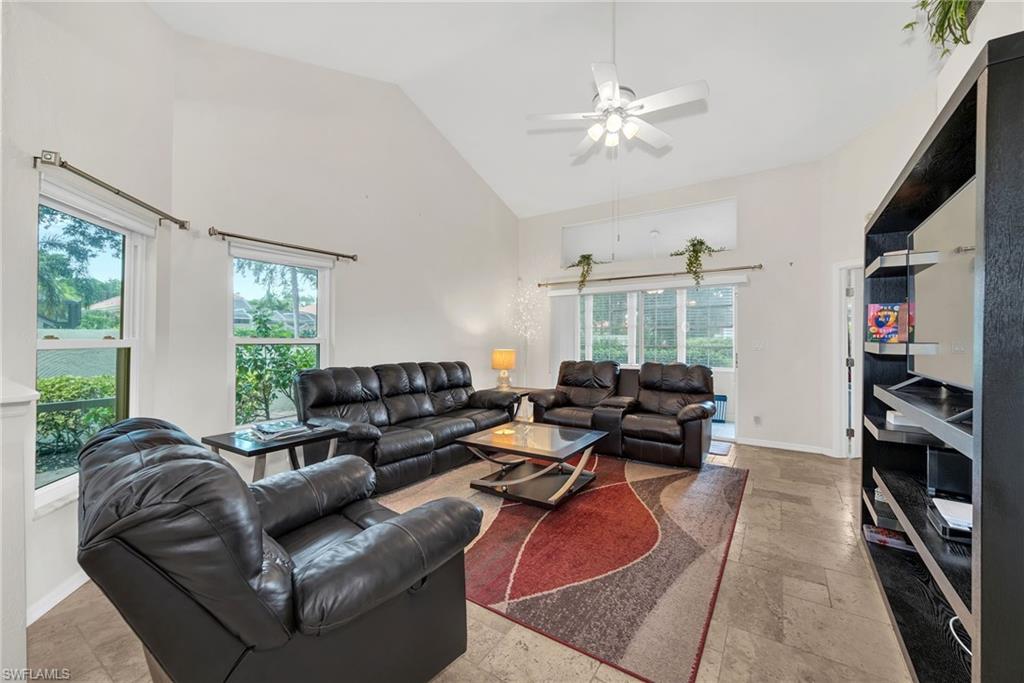 Vaulted ceiling living area featuring tile flooring, a ceiling fan, and large windows
