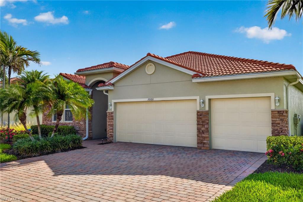 Stucco exterior residence featuring a red tile roof, paver driveway, two-car garage, and stone accents