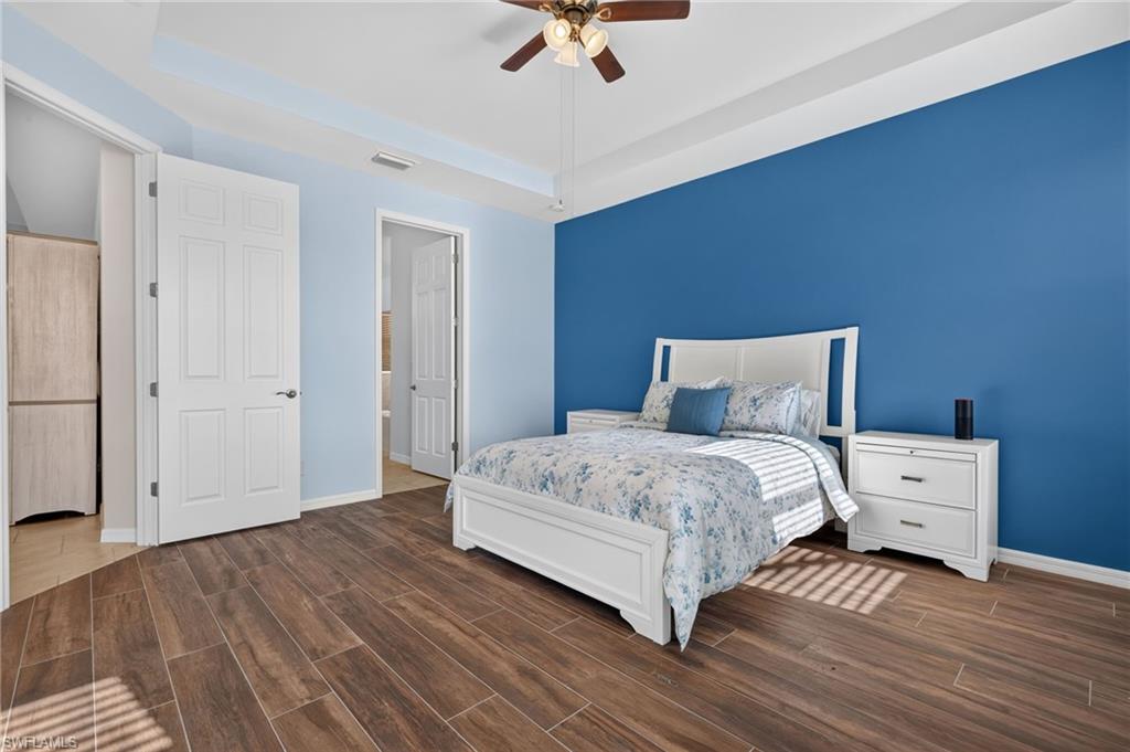Spacious room featuring wood-finish flooring, a tray ceiling, and a ceiling fan with integrated lighting
