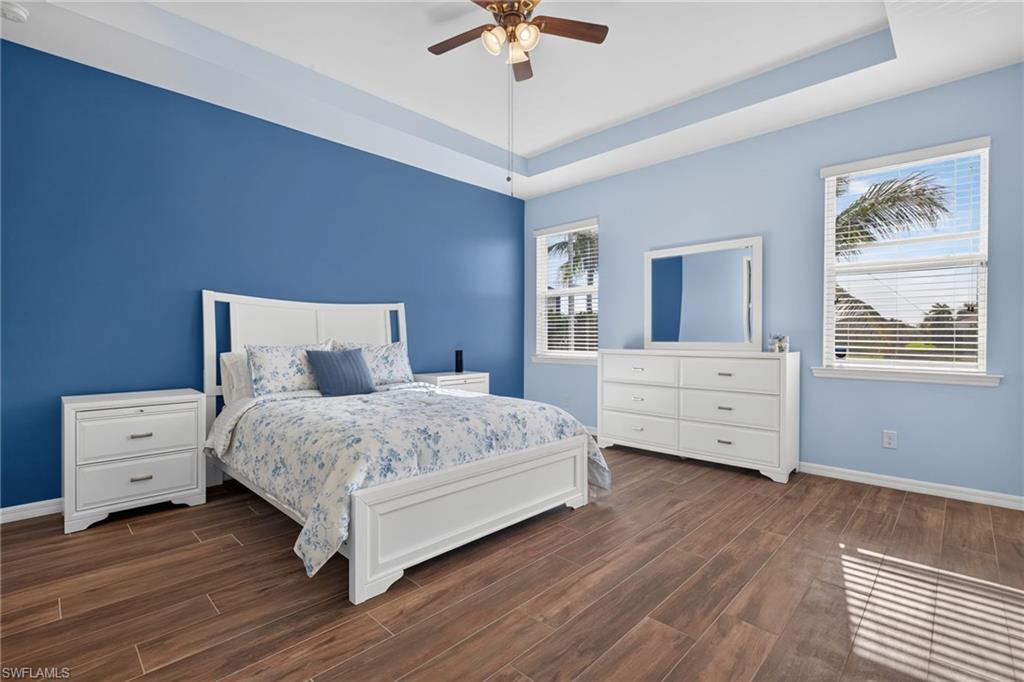 Spacious room featuring wood-finish flooring, a tray ceiling with a ceiling fan, and two windows with horizontal blinds