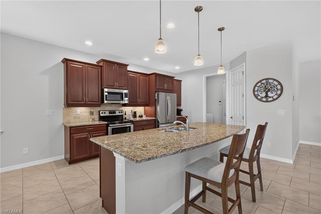 Kitchen featuring an expansive island with a double basin sink, granite countertop, pendant lighting, stainless steel appliances, and a tile backsplash