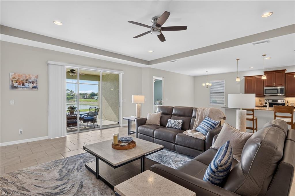 Spacious open-concept living area featuring large format tile flooring, a tray ceiling with recessed lighting and a ceiling fan, and sliding glass doors opening to a screened lanai