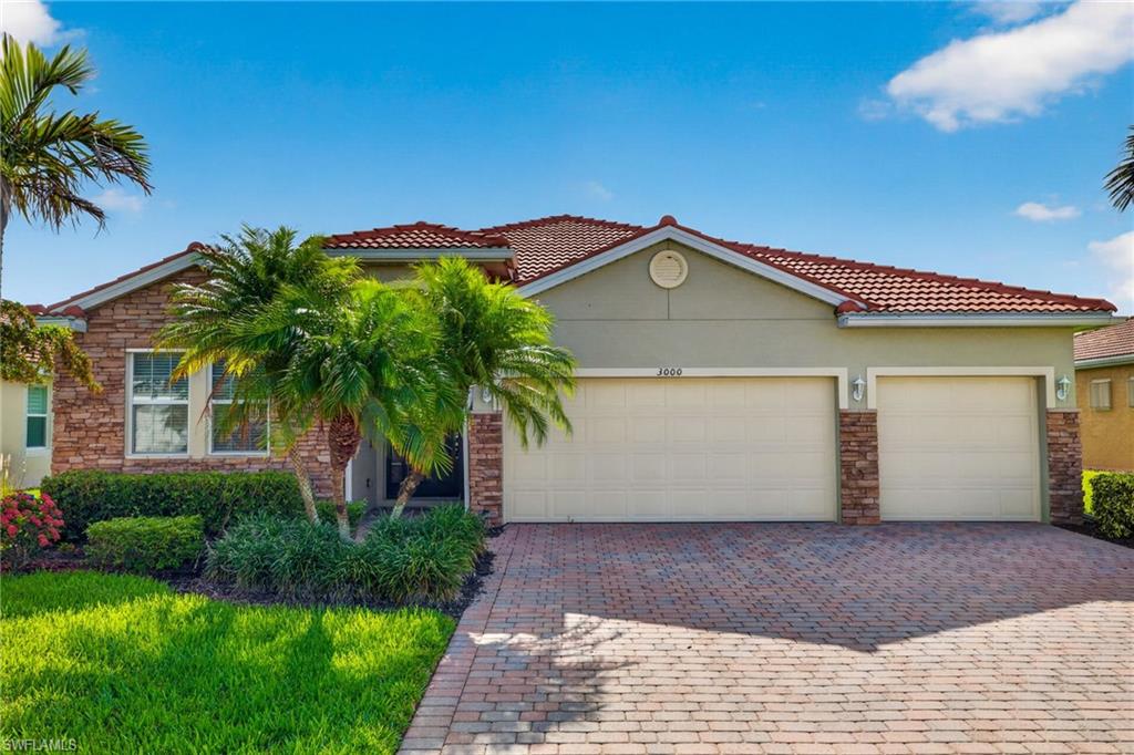 Exterior featuring a red tile roof, stone facade accents, a two-car garage, mature landscaping, and a paver driveway