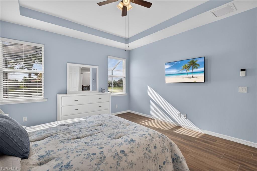 Room featuring wood-finish flooring, a tray ceiling, and a ceiling fan with light fixture