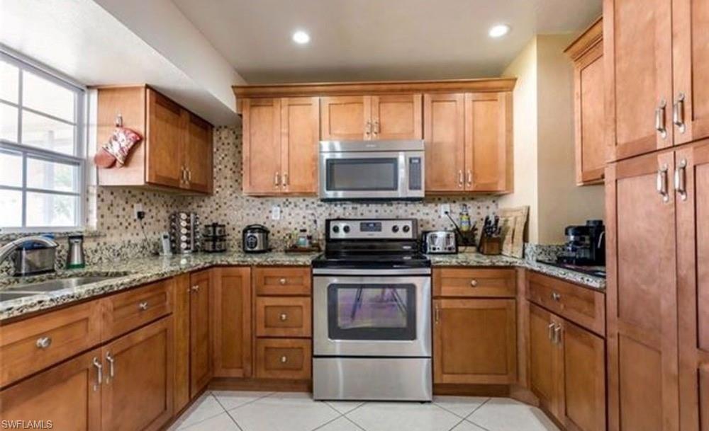 Kitchen featuring wood cabinetry, stainless steel appliances, speckled stone countertops, a tiled backsplash, and recessed lighting