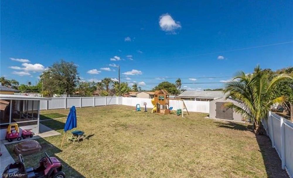 Expansive backyard featuring a screened patio, a white privacy fence, and mature palm trees