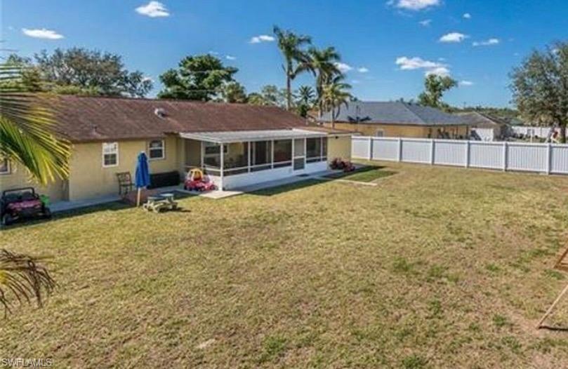 Expansive backyard featuring a white privacy fence, screened-in patio, and mature palm trees