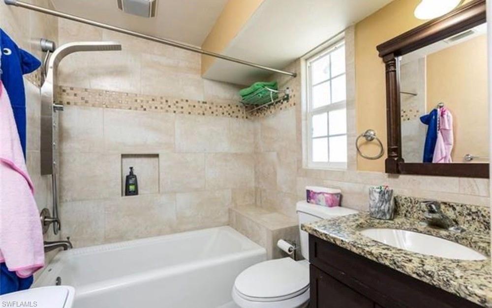 Bathroom featuring a white bathtub, a tiled shower surround with an integrated niche, and a vanity with a granite-style countertop