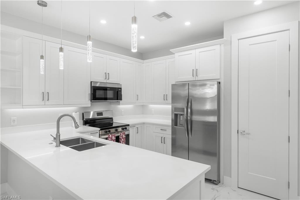 Contemporary kitchen featuring white shaker cabinetry, stainless steel appliances, white countertops, and three cylindrical pendant lights