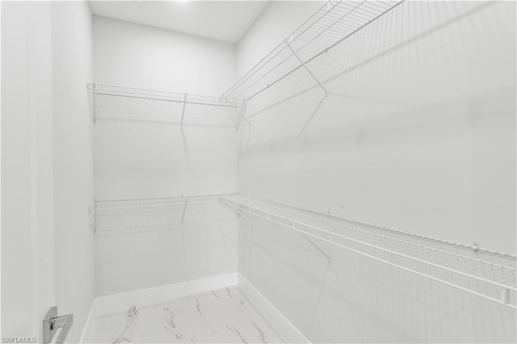 Walk-in closet featuring white wire shelving on multiple walls, a light fixture, and marble-look floor tiles
